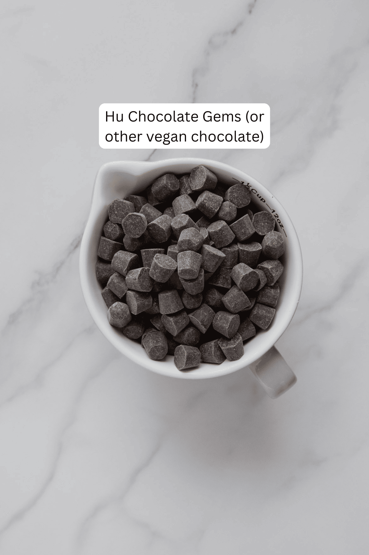 Chocolate gems in a white mug with a white marble background.