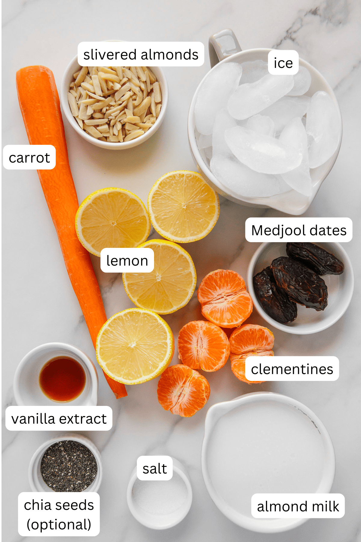 Ingredients of a carrot smoothie with a white marble background.