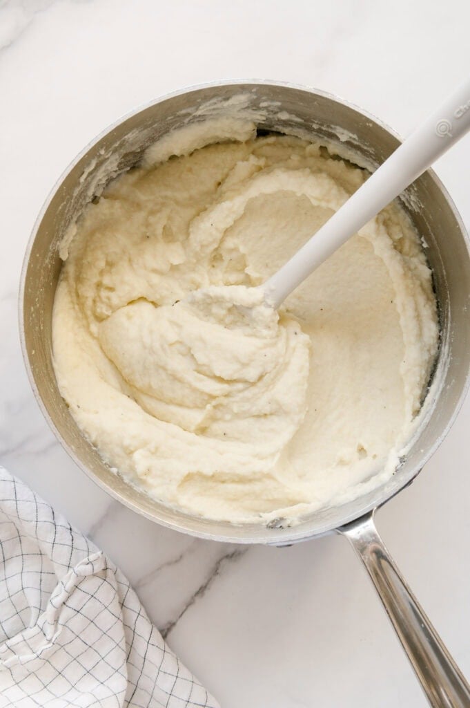Mashed potatoes in a small saucepan with a white marble background.