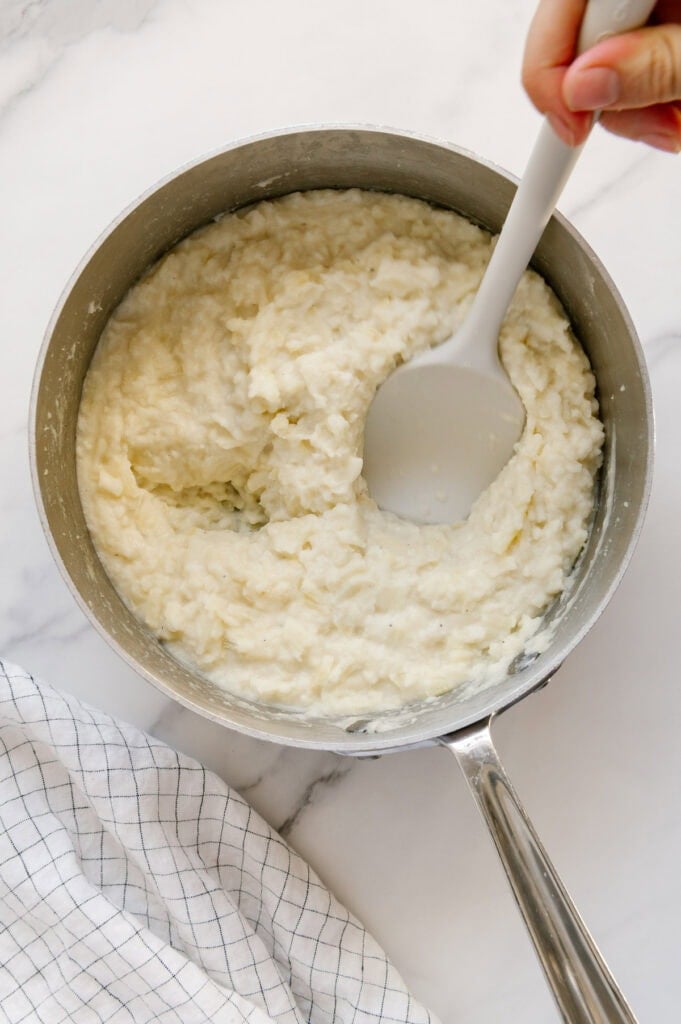 A silicone spatula being used to mash potatoes in a saucepan.