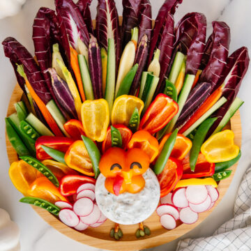 Vegetables arranged to look like a colorful turkey on a circular wooden platter.