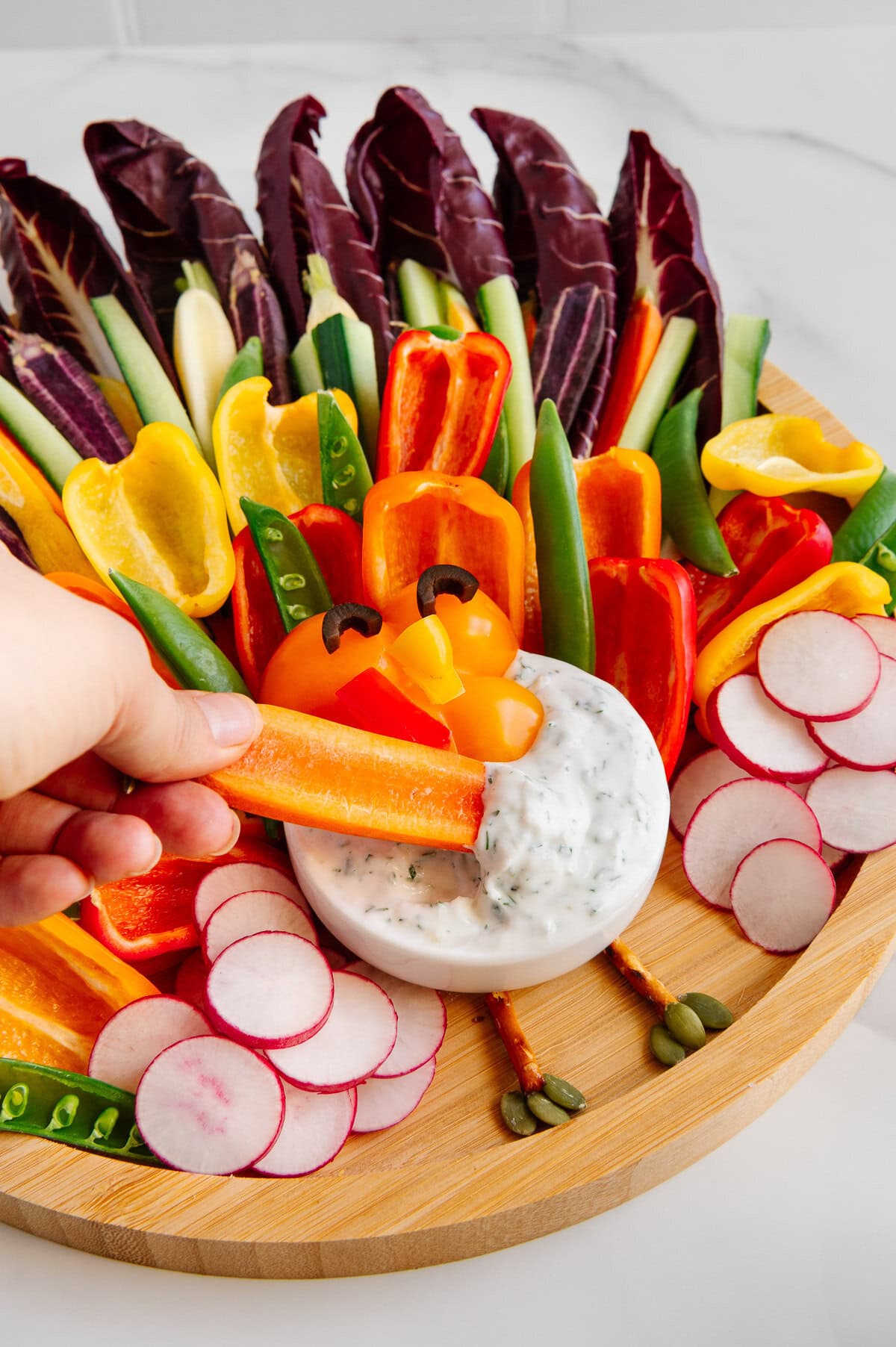 A hand dipping a bell pepper into vegan ranch on a Thanksgiving turkey veggie platter.
