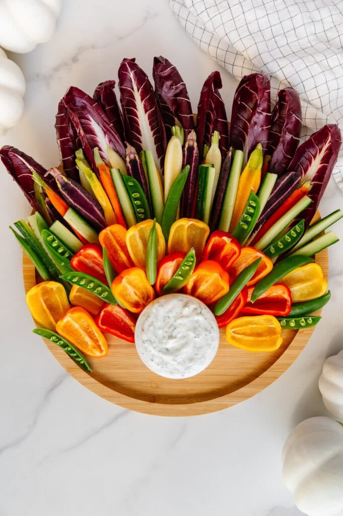 Circular wooden platter with a small bowl of vegan ranch at the bottom and fresh veggies arranged like a colorful turkey.