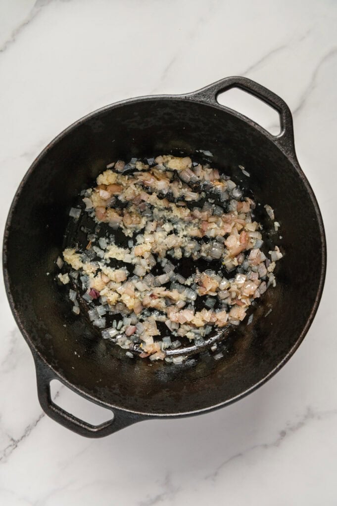 Sautéed shallots and garlic in a cast iron skillet with a white marble background.