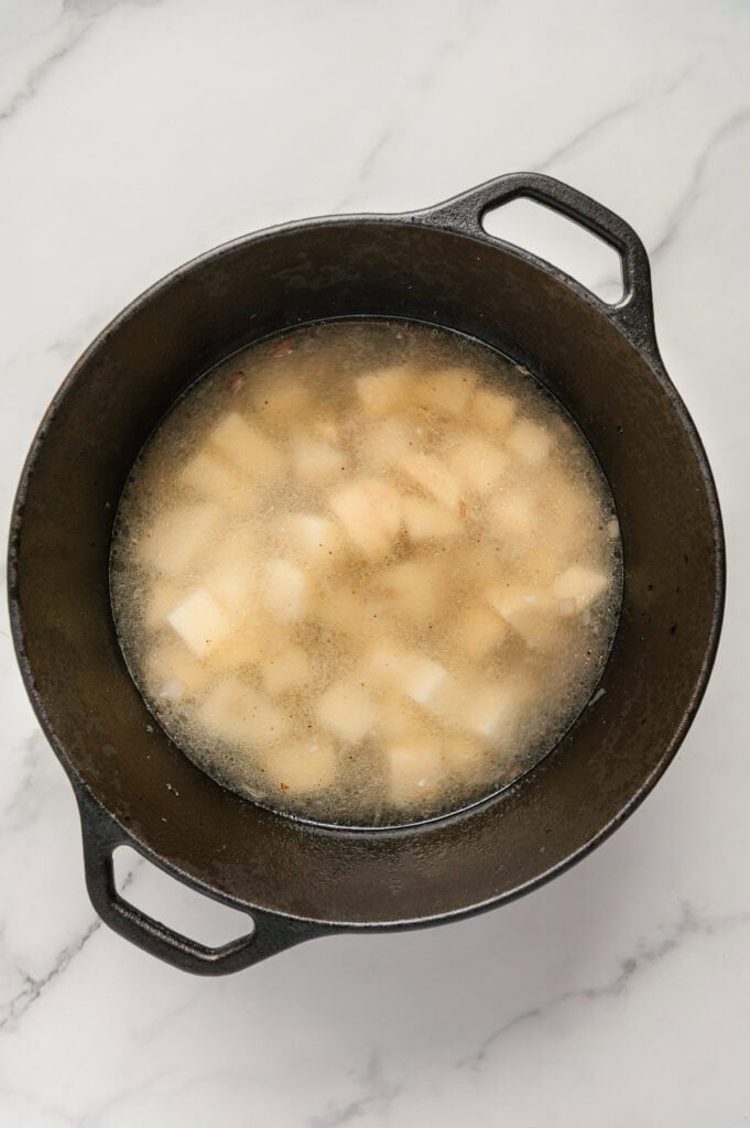 Chopped russet potatoes in a dutch oven covered with water with a white marble background.