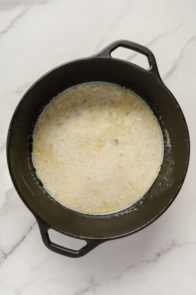 Vegan potato soup in a dutch oven prior to being blended with a white marble background.