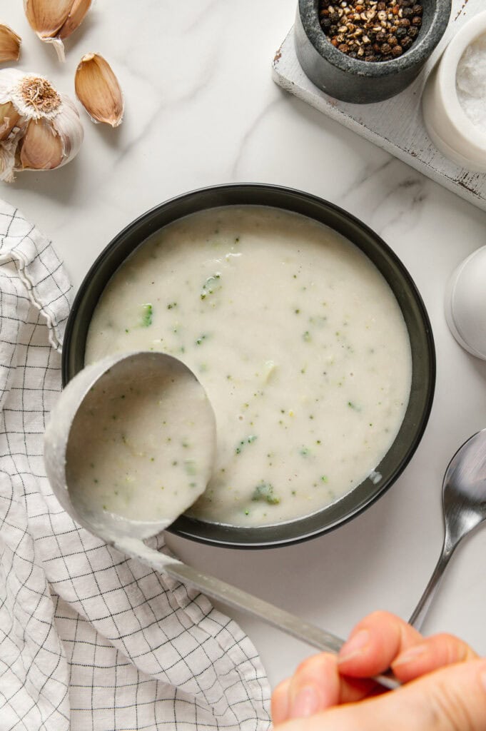 A hand using a ladle to serve vegan potato soup in a black bowl.