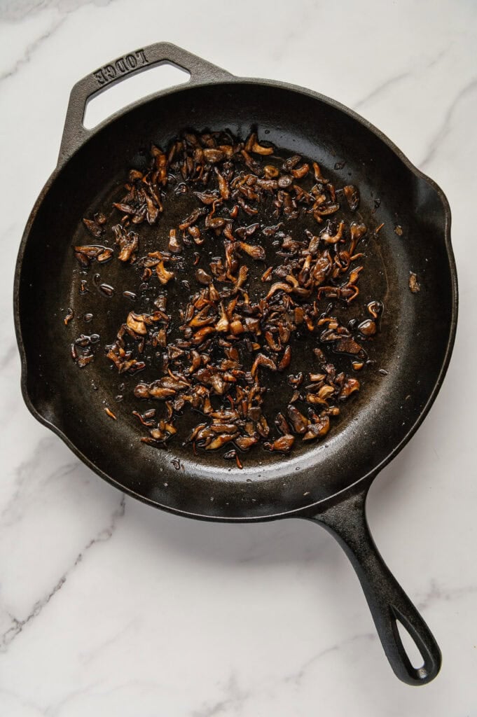 Vegan mushroom bacon in a cast iron skillet with a white marble background.