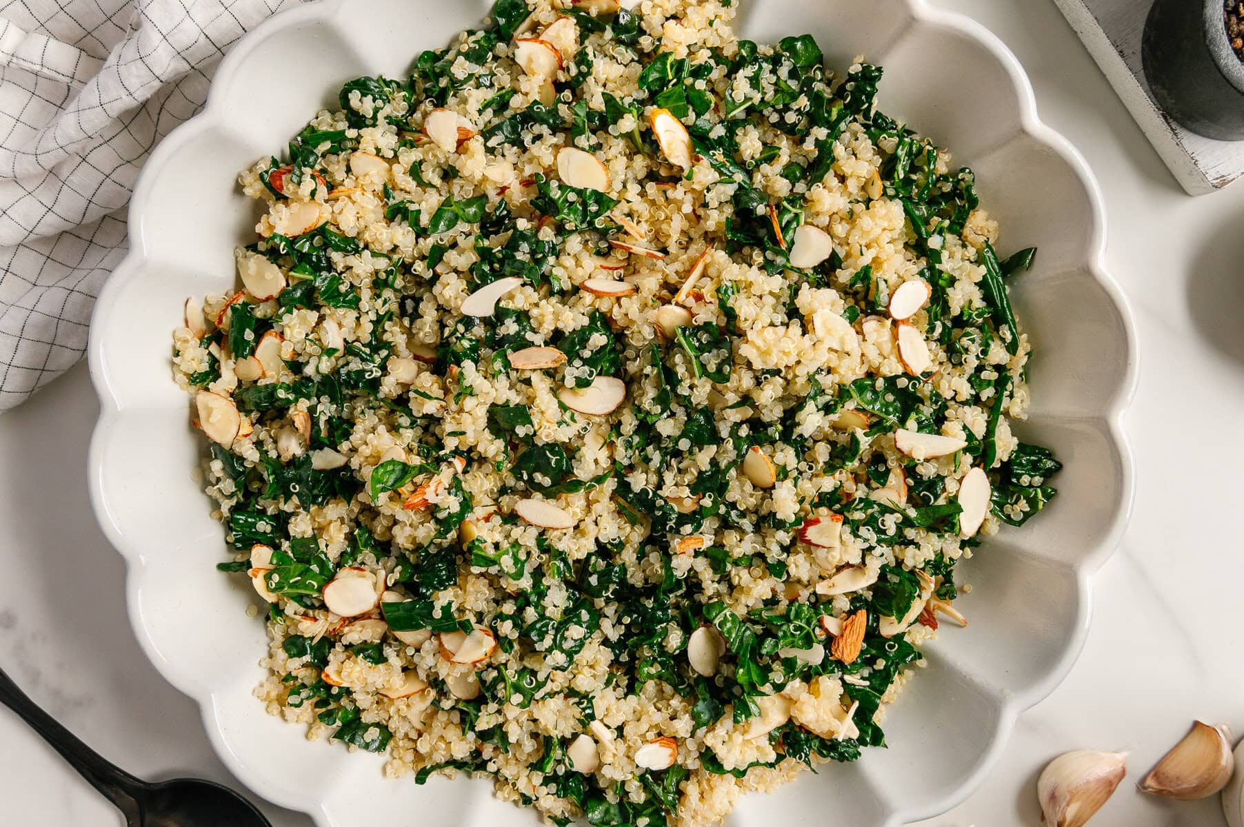 Kale quinoa salad in a white bowl with a white marble background.