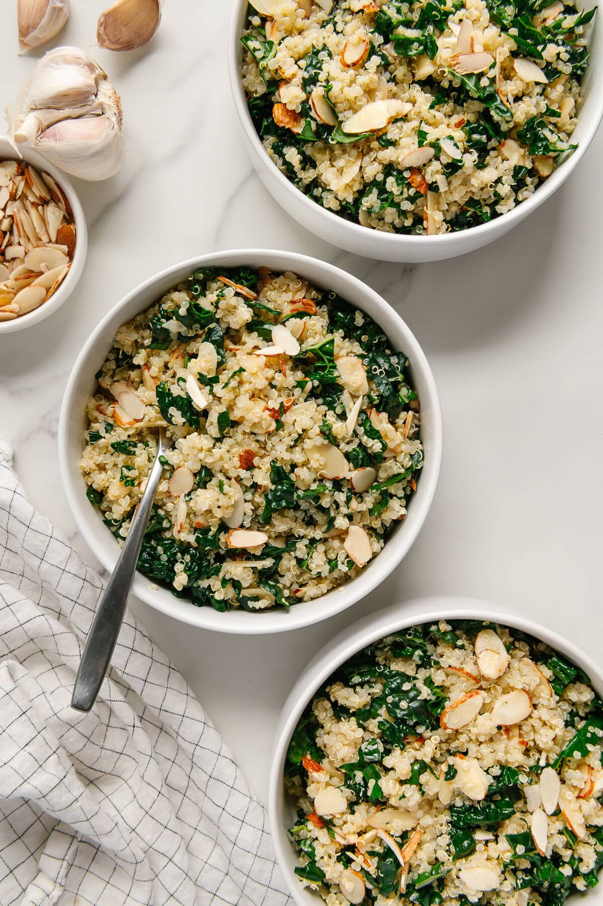 Kale quinoa salad in small white bowls with a white marble background.