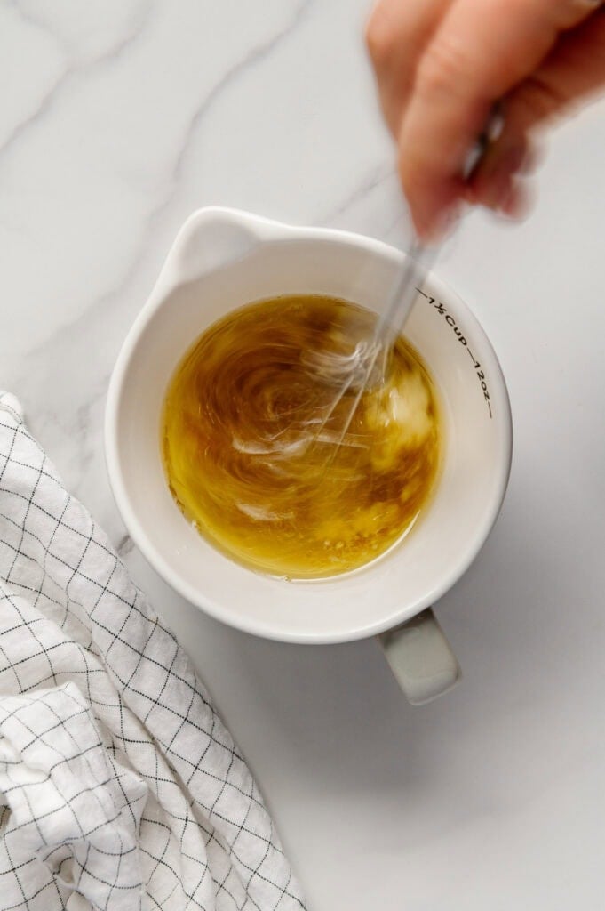 A hand stirring ingredients of a lemon garlic dressing in a white measuring cup.