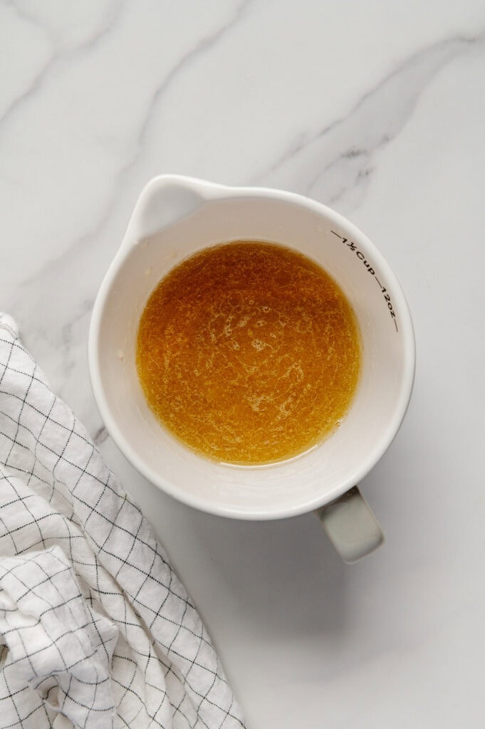 A lemon garlic dressing in a white measuring cup with a white marble background.