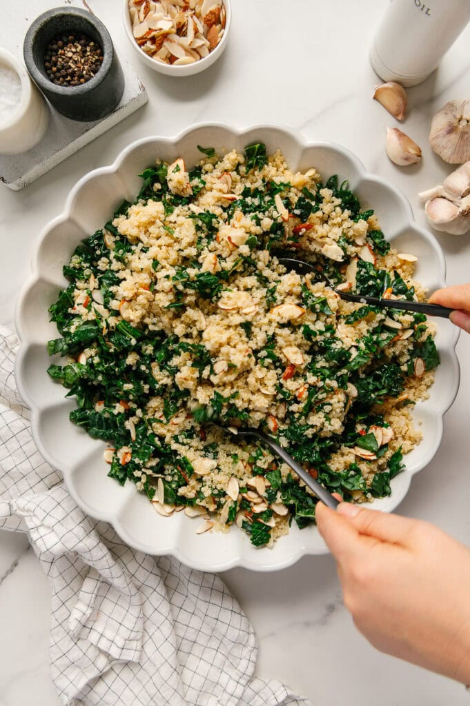 Two hands using utensils to toss a kale quinoa salad.
