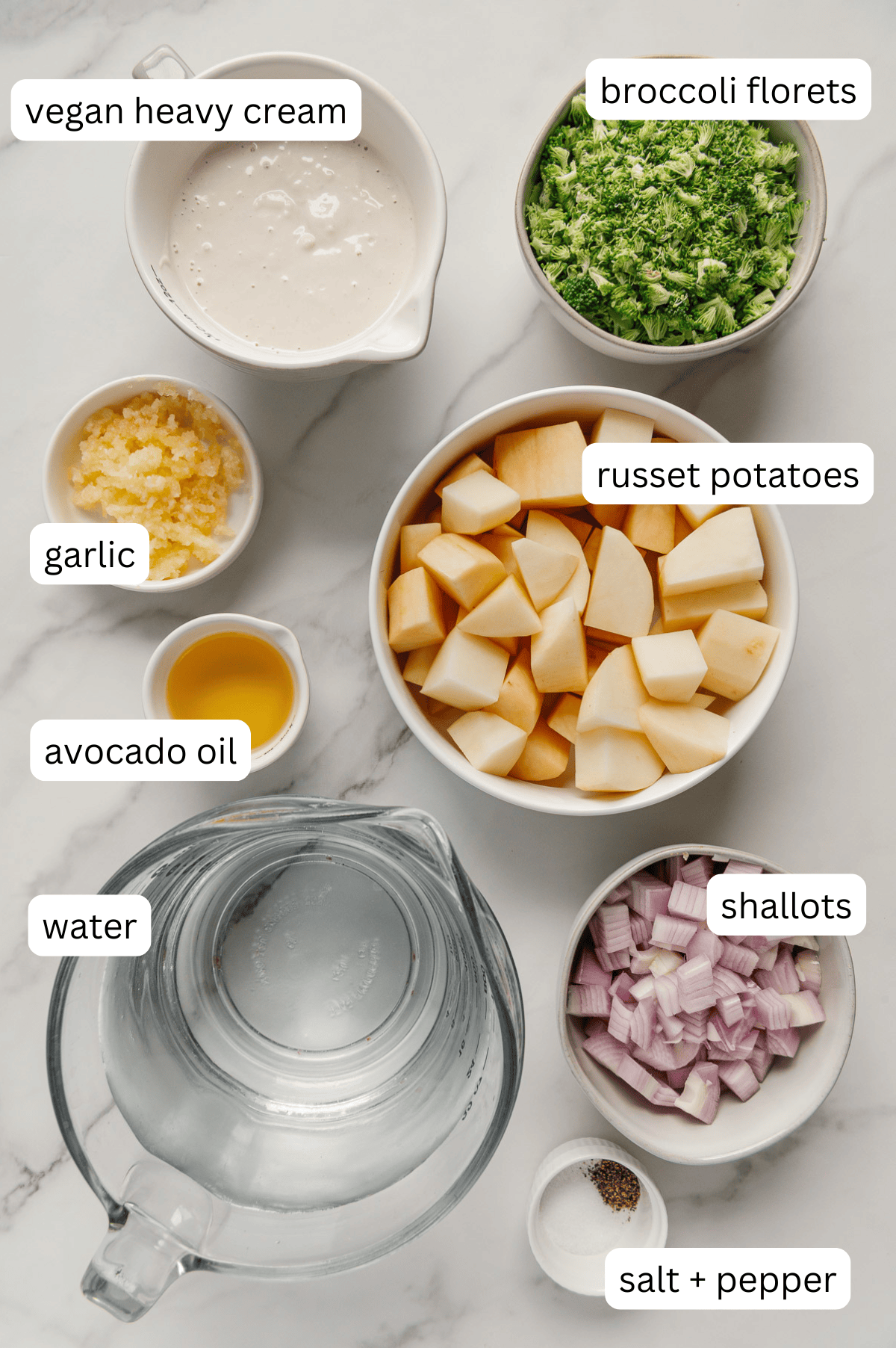 Ingredients of vegan potato soup in separate bowls with a white marble background.