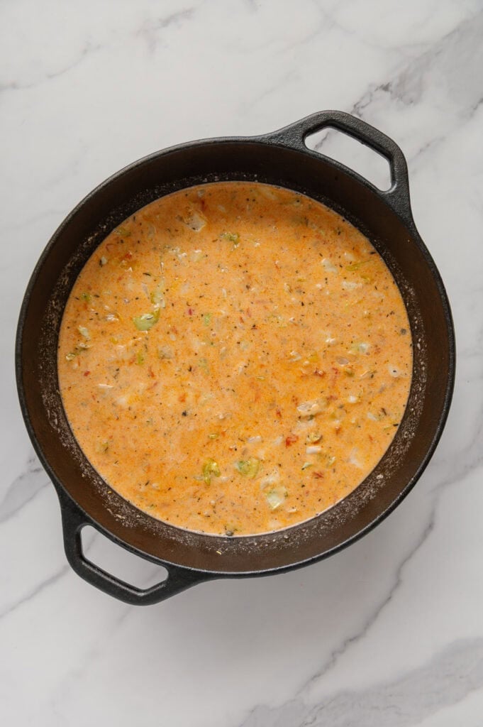 Vegan cabbage soup in a dutch oven while still cooking with a white marble background.