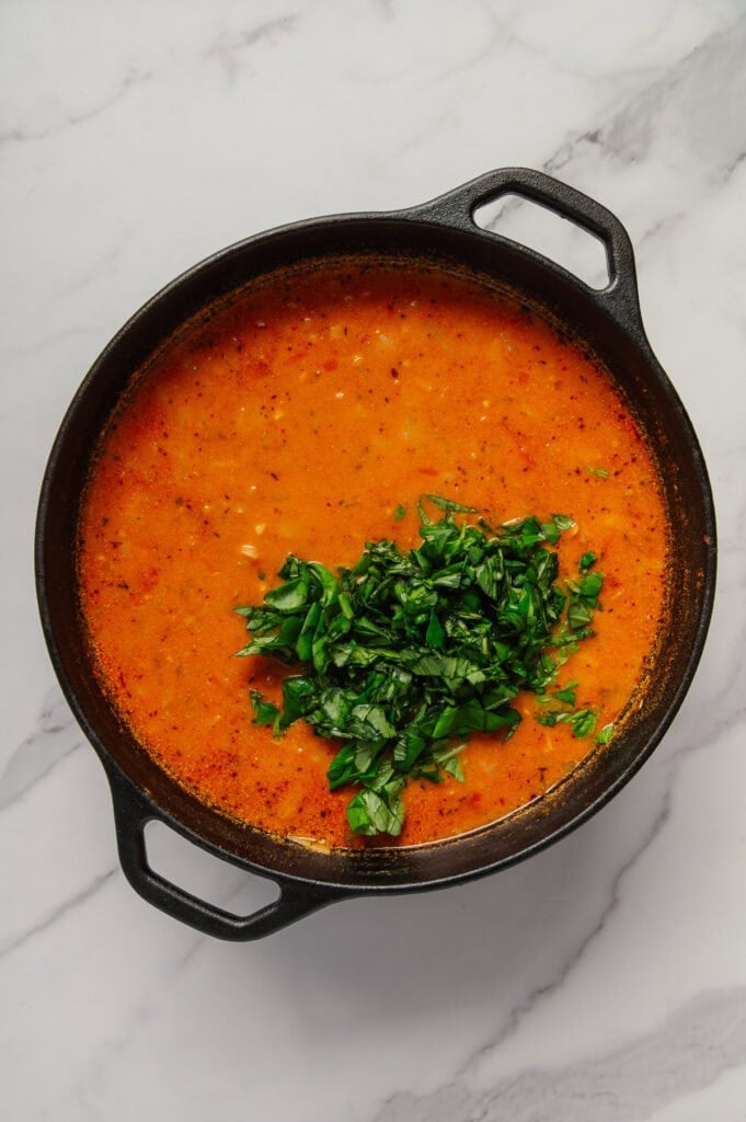 Fresh basil added to vegan cabbage soup in a dutch oven with a white marble background.