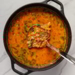 Vegan cabbage soup in a dutch oven with a ladle scooping up a serving.