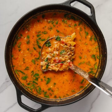 Vegan cabbage soup in a dutch oven with a ladle scooping up a serving.