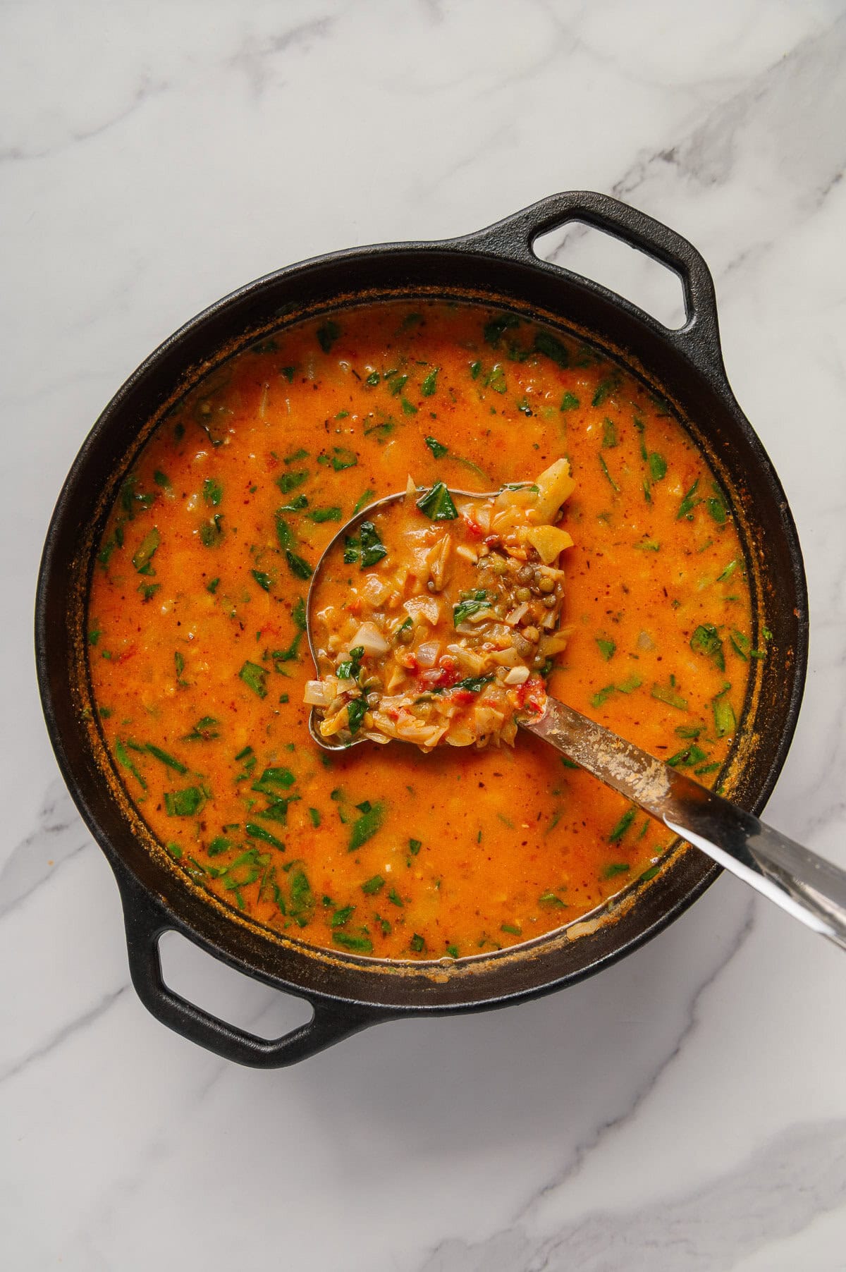 Vegan cabbage soup in a dutch oven with a ladle scooping up a serving.