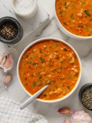 Vegan cabbage soup served in two white bowls with a white marble background.