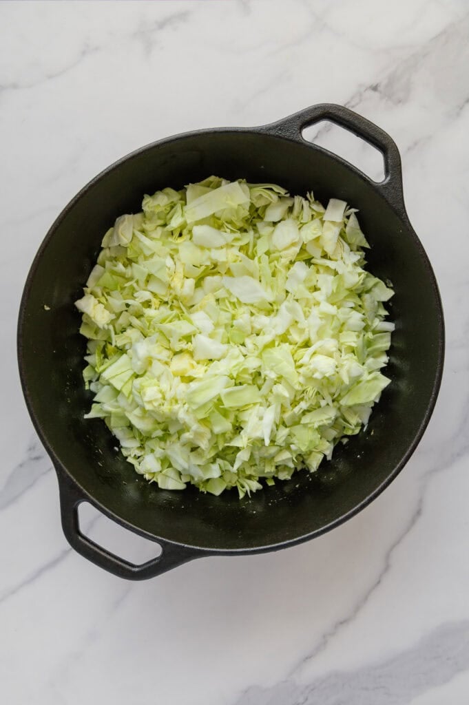Chopped green cabbage in a dutch oven with a white marble background.