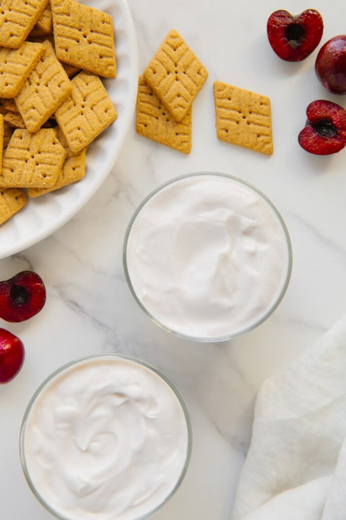 Overhead photo of yogurt in small glasses next to Simple Mills diamond-shaped cookies with a white marble background.