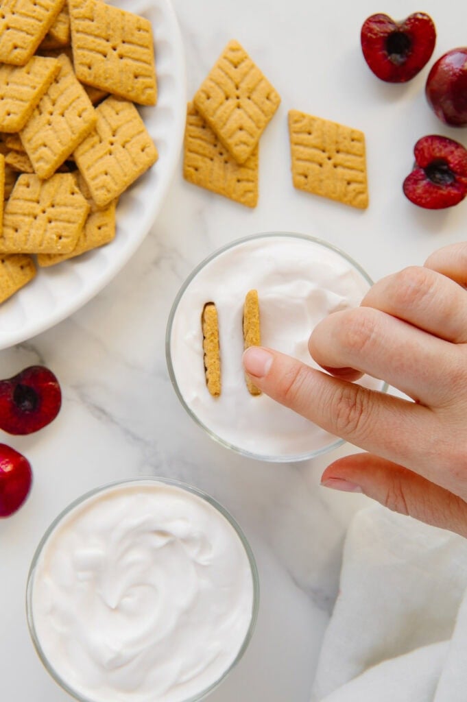 A hand placing Simple Mills cookies into a glass of yogurt.