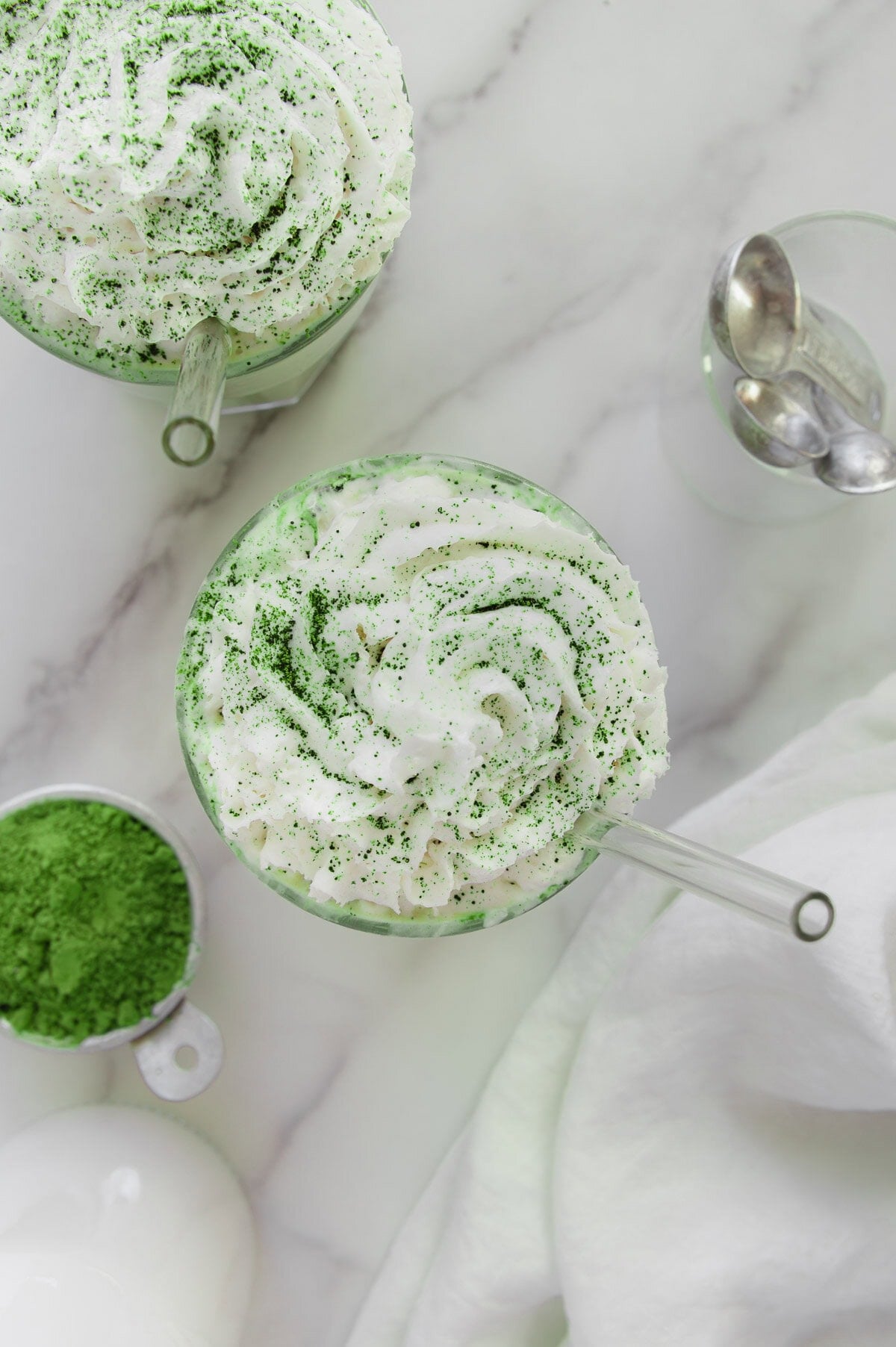 An overhead angle of a matcha smoothie topped with vegan whipped cream and sifted matcha powder with a white marble background.