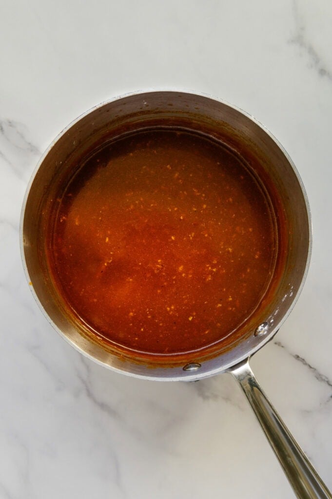Enchilada sauce in a sauce pan with a white marble background.