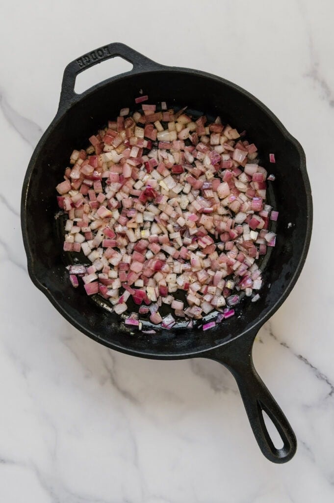 Sautéed onions and garlic in a cast iron skillet with a white marble background.