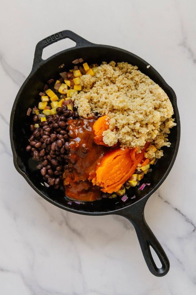 Cooked quinoa, cooked sweet potato, enchilada sauce and black beans added on top of sautéed yellow squash, onions and garlic in a cast iron skillet.