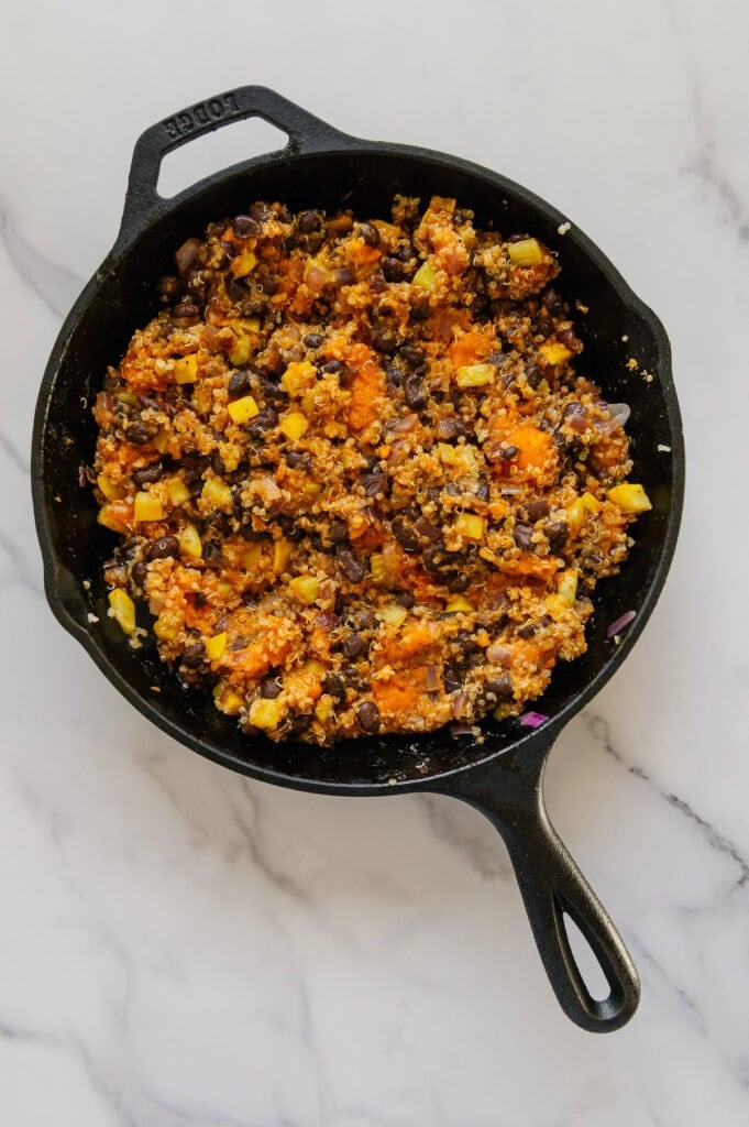 Enchilada stuffing mixture in a cast iron skillet with a white marble background.