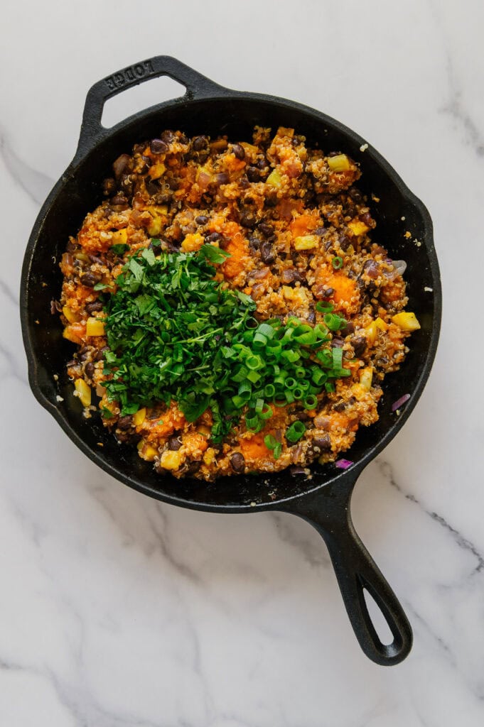 Fresh cilantro added to the enchilada stuffing mixture in a cast iron skillet.