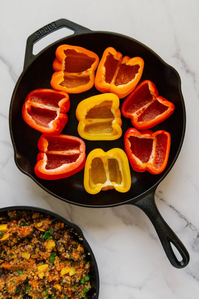 Halve red, yellow and orange bell peppers arranged in a cast iron skillet with a white marble background.