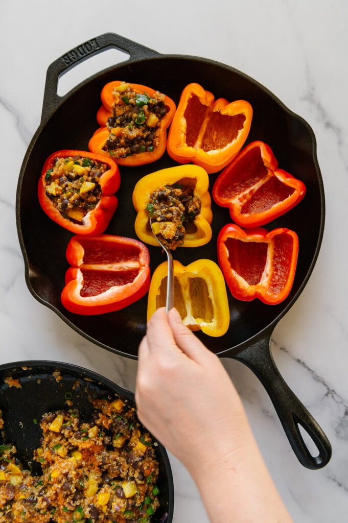 A hand spooning enchilada stuffing mixture into bell pepper halves in a cast iron skillet.