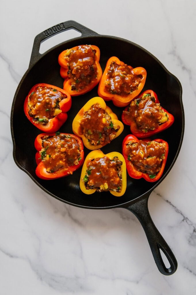 Stuffed bell peppers topped with homemade enchilada sauce in a cast iron skillet.