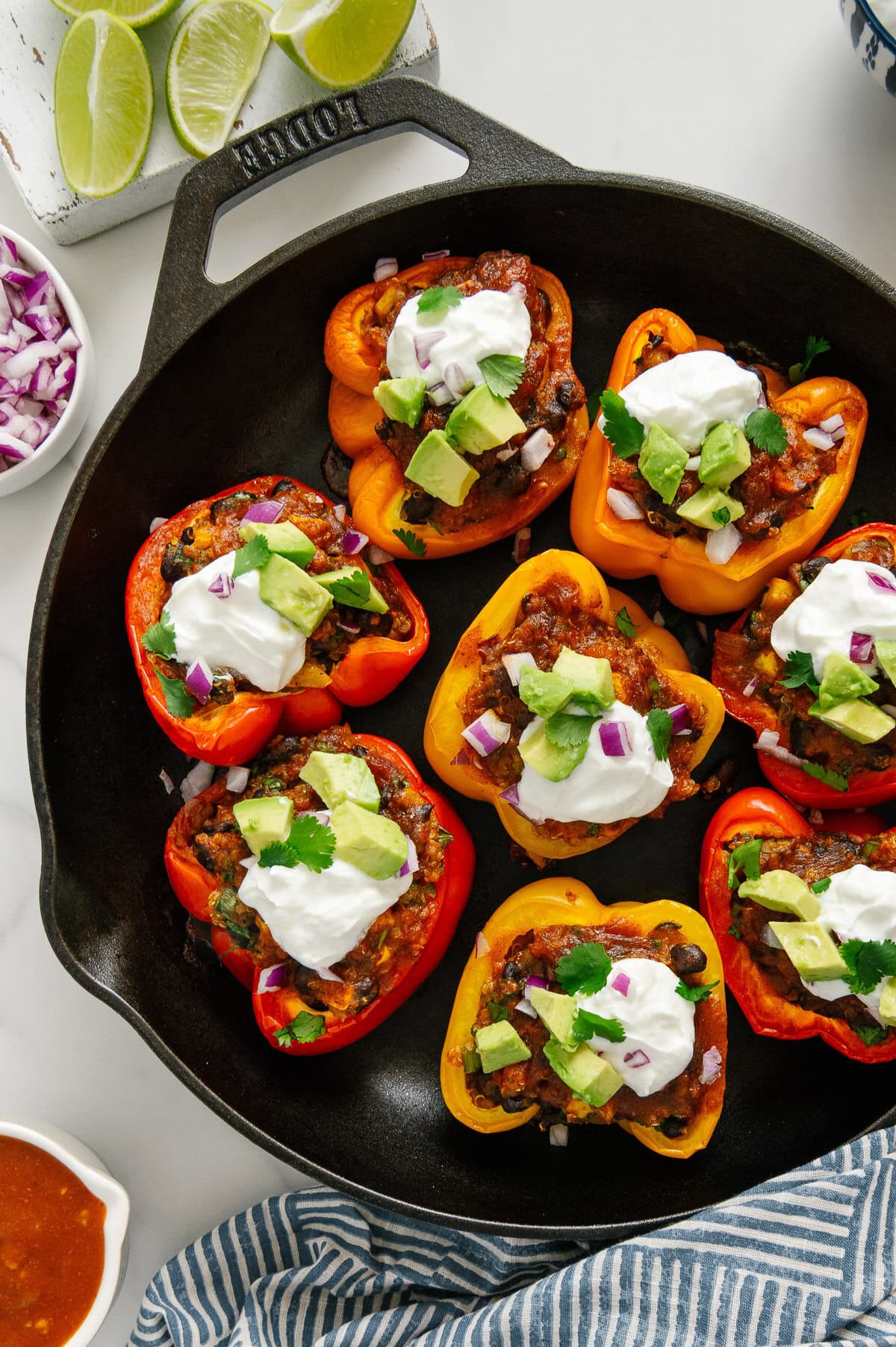 Enchilada stuffed bell peppers in a cast iron skillet topped with vegan sour cream, diced avocado, fresh cilantro and red onions.