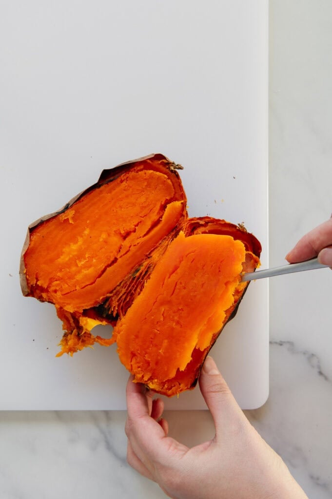 Hands removing the skin from a cooked sweet potato cut in half.
