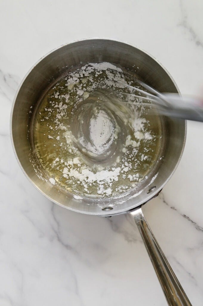 A whisk whisking arrowroot powder into olive oil in a sauce pan.