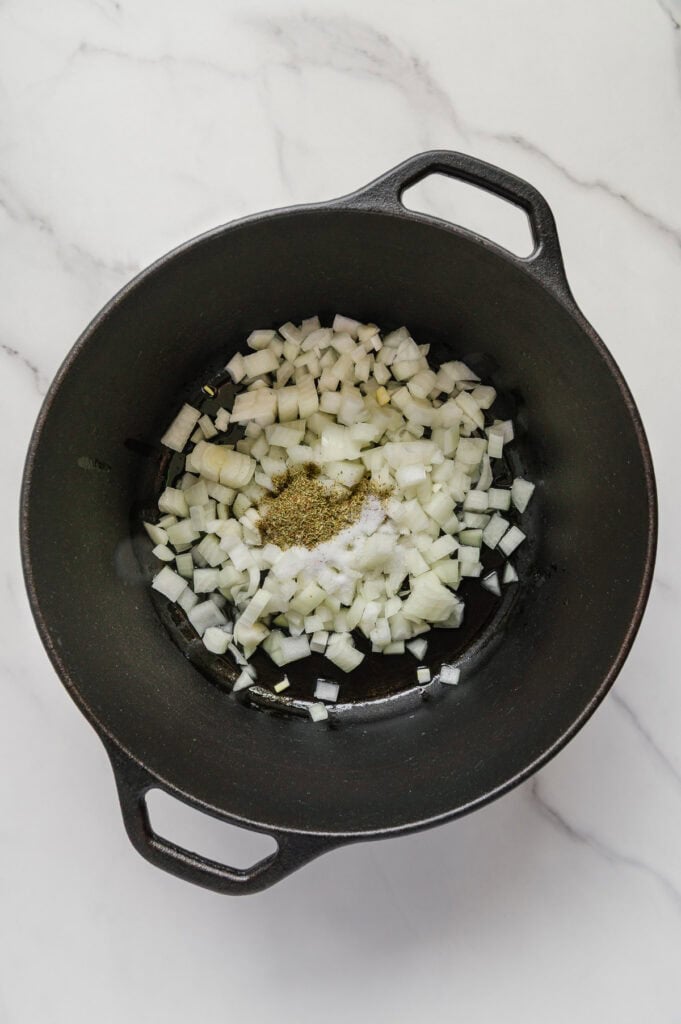 A black pot on a marble surface contains chopped onions, salt, and pepper-essential ingredients for starting a flavorful vegan Italian wedding soup.
