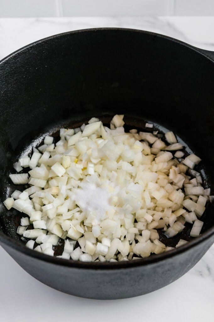 Diced onions and a pile of salt in a black cast iron pot, ready to be cooked.