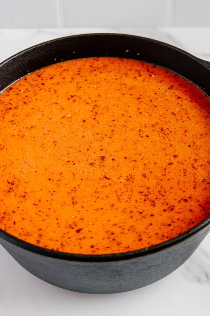 A black pot filled with a vibrant orange, oily broth with red specks, sitting on a white marble surface.