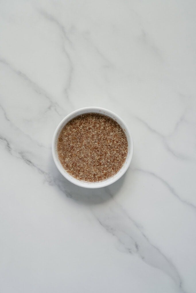 A small white bowl filled with a brown, grainy mixture sits on a white marble surface.