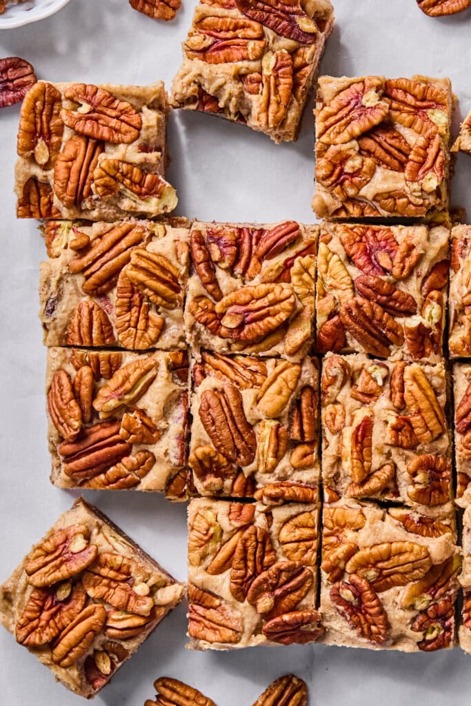 Top view of pecan bars cut into squares on parchment paper, with whole pecans on top and a few loose pecans around the bars.