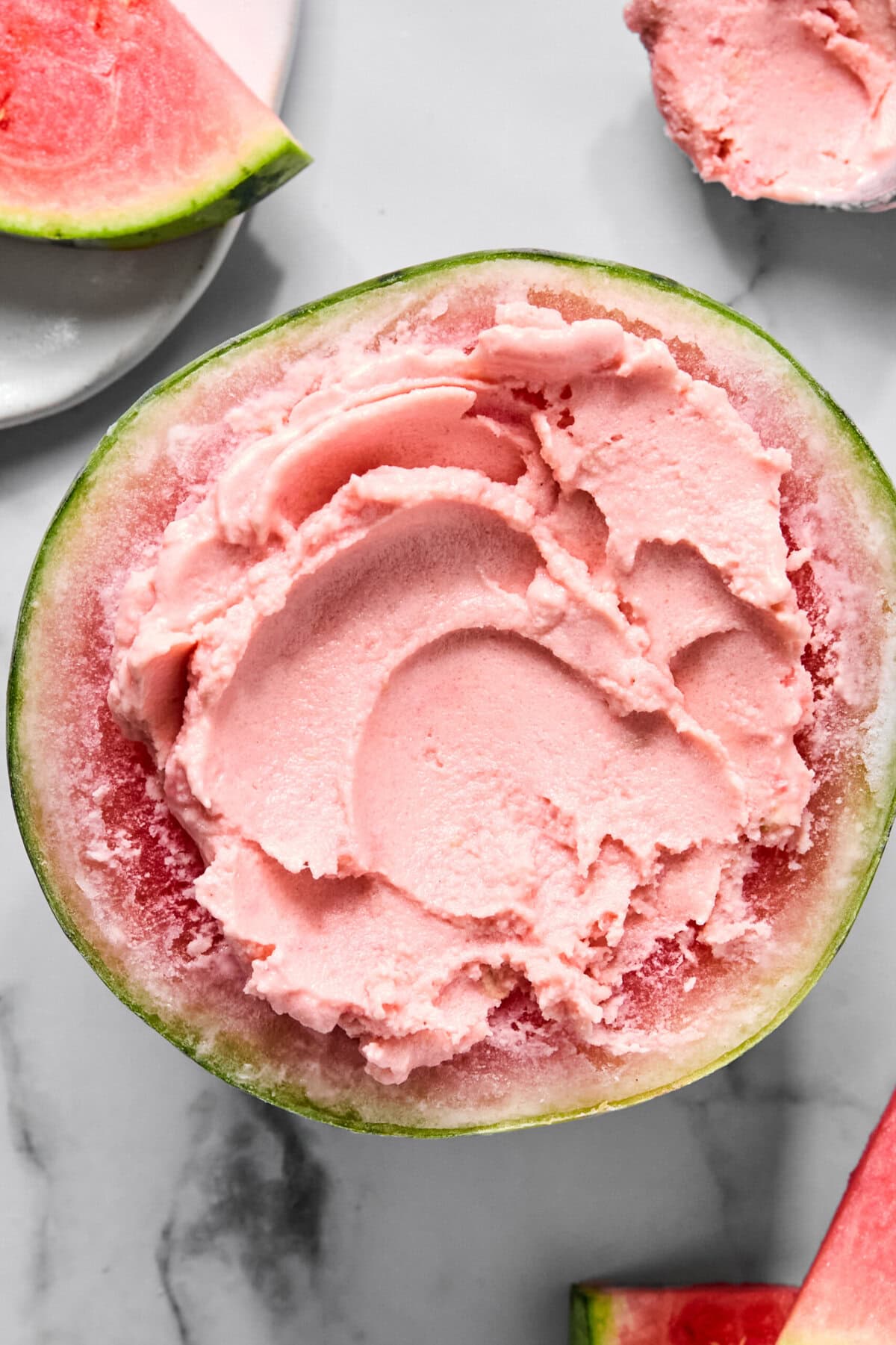 A halved watermelon filled with smooth pink watermelon sorbet, surrounded by watermelon slices on a white surface-just like a viral TikTok watermelon ice cream recipe brought to life.