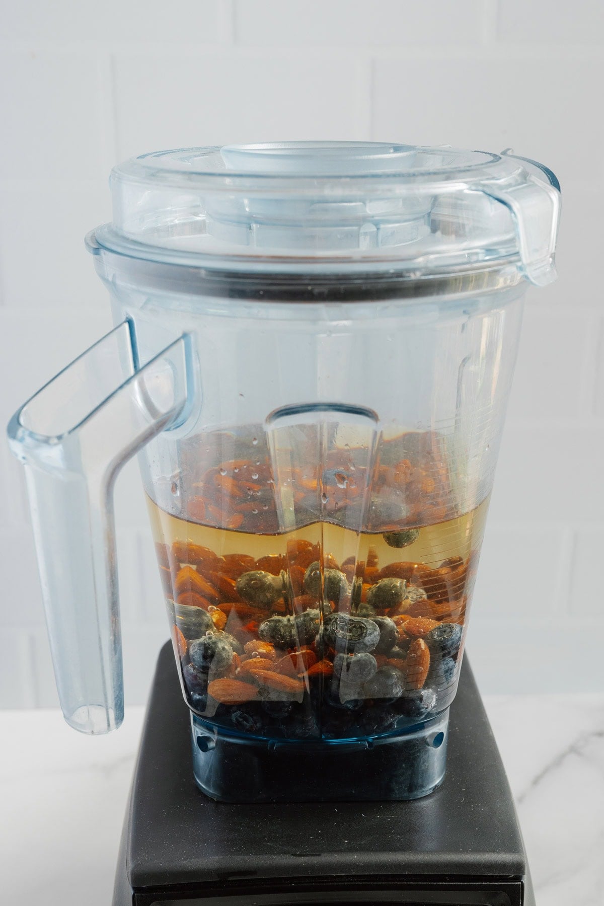A blender container filled with blueberries, chopped carrots, and liquid-such as naturally sweetened blueberry almond milk-sits on a black blender base against a light background, highlighting this deliciously dairy-free blend.