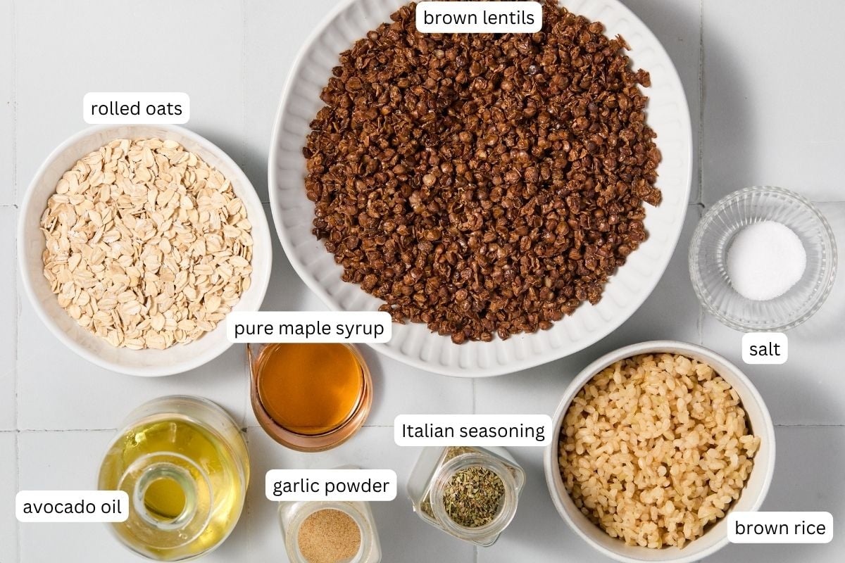A bowl of cooked brown lentils, perfect for Vegan Meatballs, is surrounded by bowls of rolled oats, brown rice, salt, Italian seasoning, garlic powder, pure maple syrup, and a small carafe of avocado oil-all labeled and ready to help you create delicious vegan dishes.