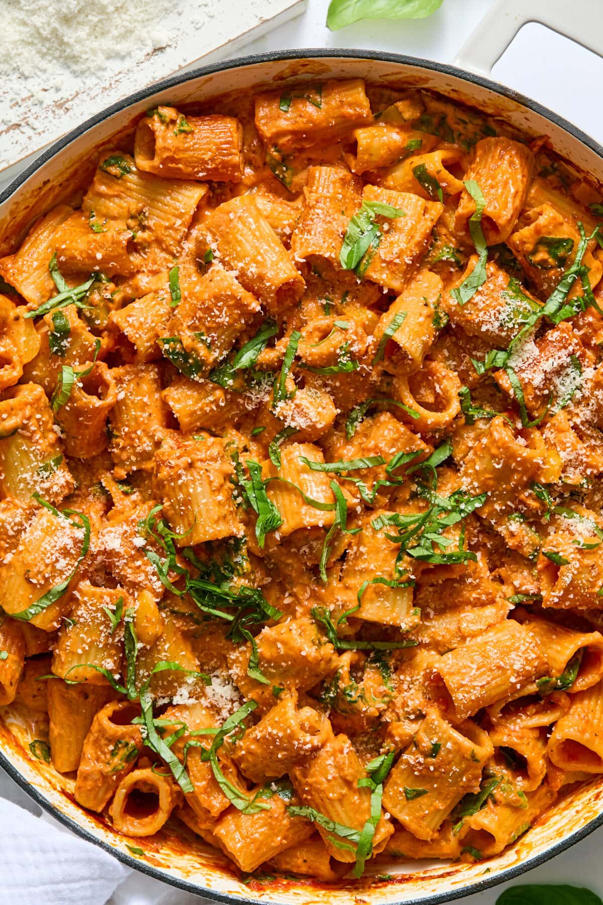 A skillet filled with rigatoni pasta in creamy tomato sauce, topped with grated parmesan cheese and chopped fresh basil.