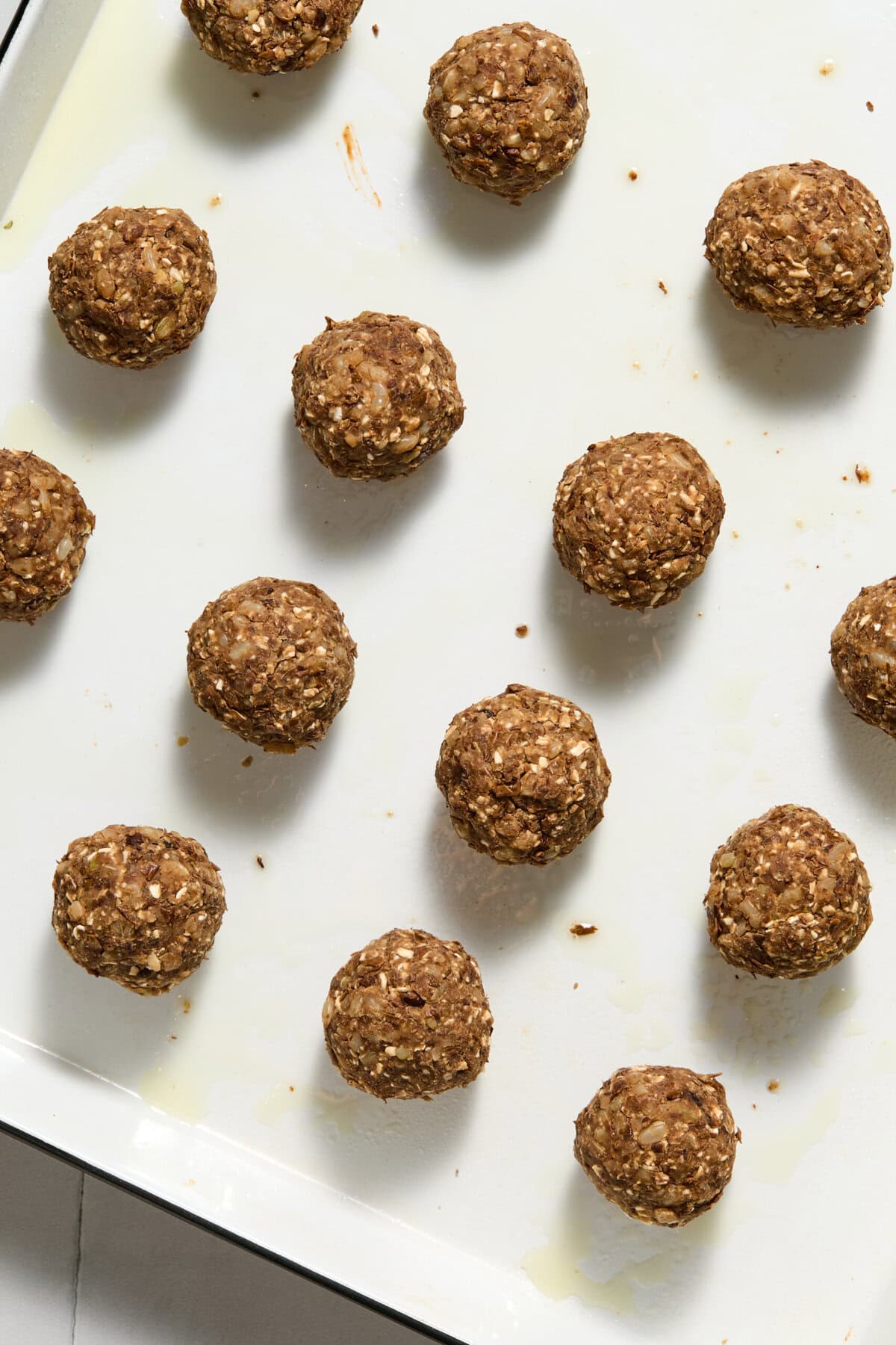 Round oat and nut energy bites evenly spaced on a white baking sheet, ready to be baked or served.