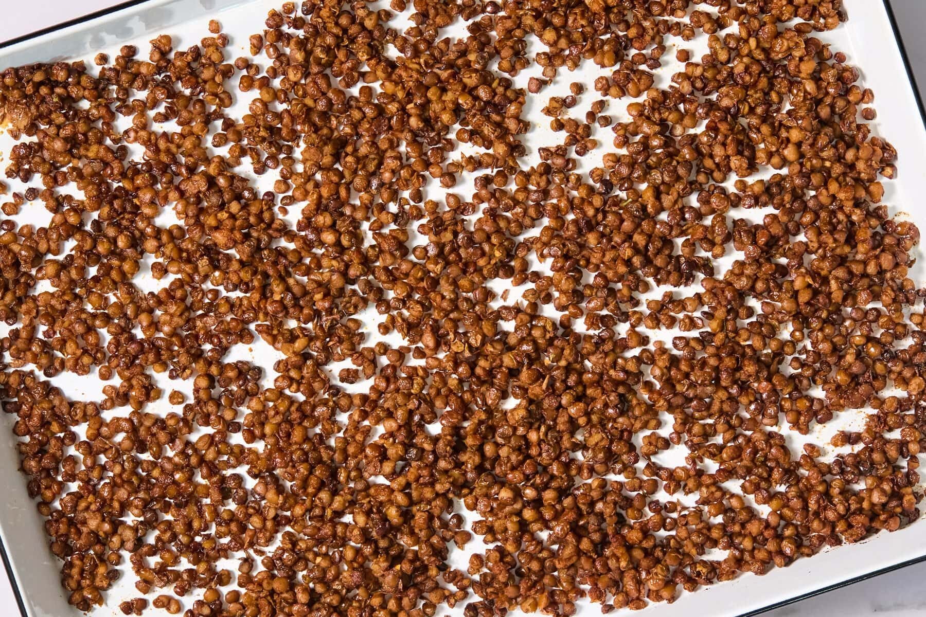 Toasted lentils scattered in a single layer on a white baking sheet.